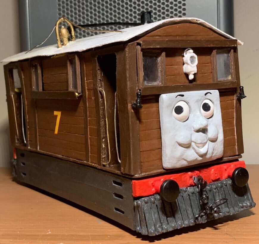 Here is my model of the character, Toby the Tram Engine. Like with Rusty, he is made of mostly cardboard with wooden coffee stirrers for the planks. The number 7 decals are hand cut from red and yellow sheets of vinyl. The cowcatchers are made from plastic with sticker gems for the rivets. This time, I gave him the ability to have his eyes posed using sticky tack on the faces.